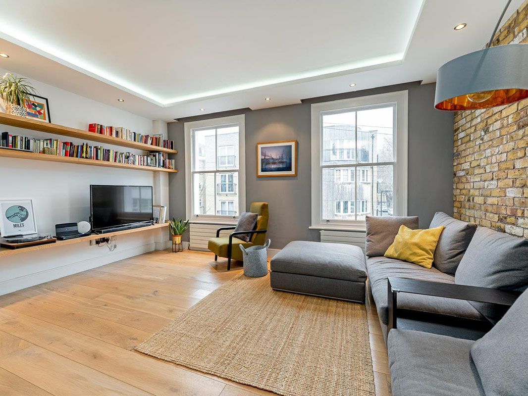 Living room renovation with exposed London stock brick wall, bespoke oak shelving and recessed cove lighting, Hackney London