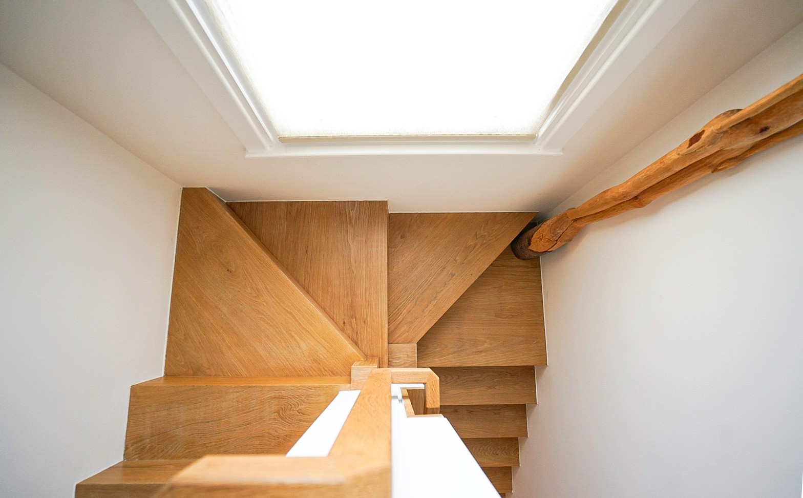 Top-down view of a bespoke oak staircase with natural timber handrail, illuminated by a flush skylight above, Islington London