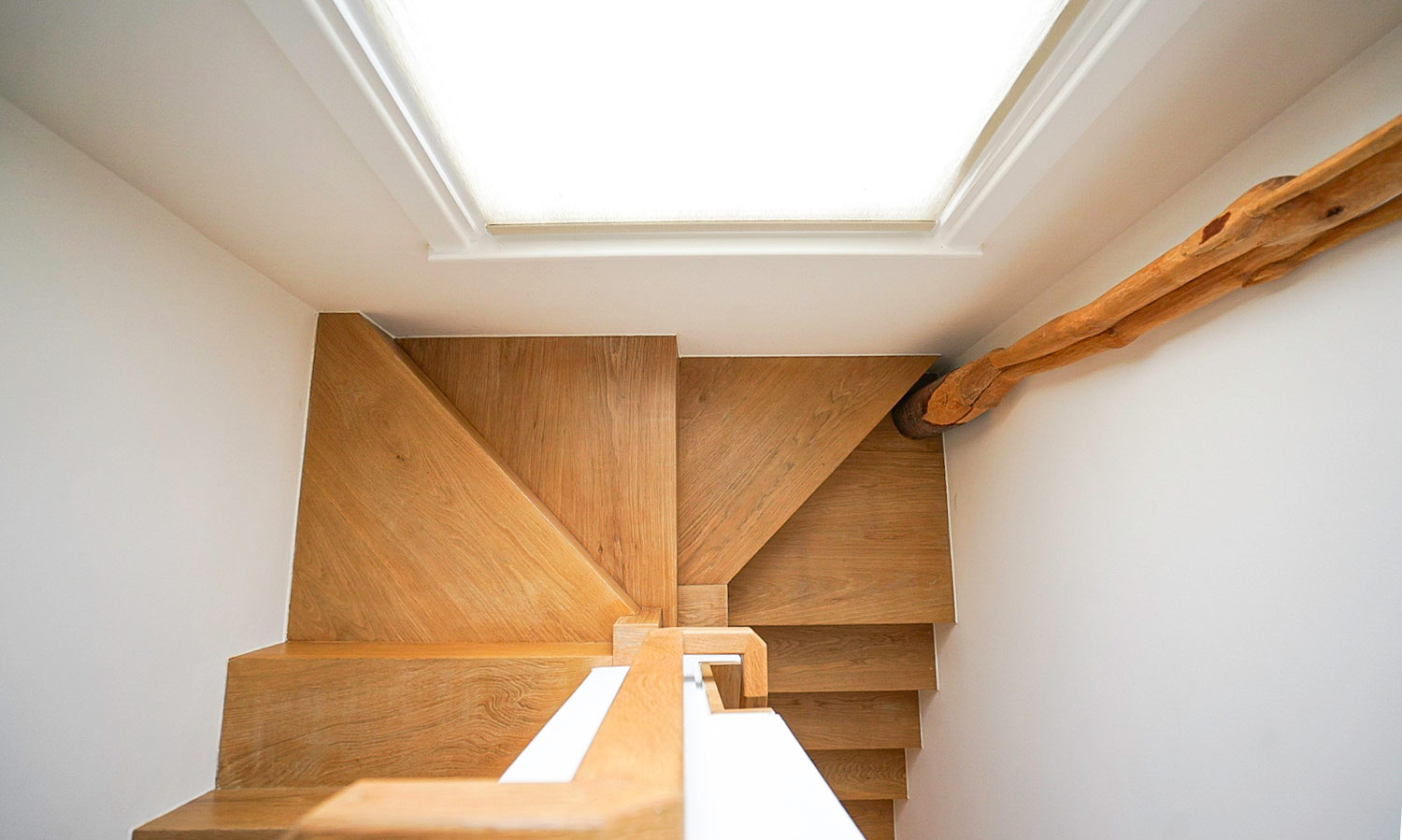 Top-down view of a bespoke oak staircase with natural timber handrail, illuminated by a flush skylight above, Islington London
