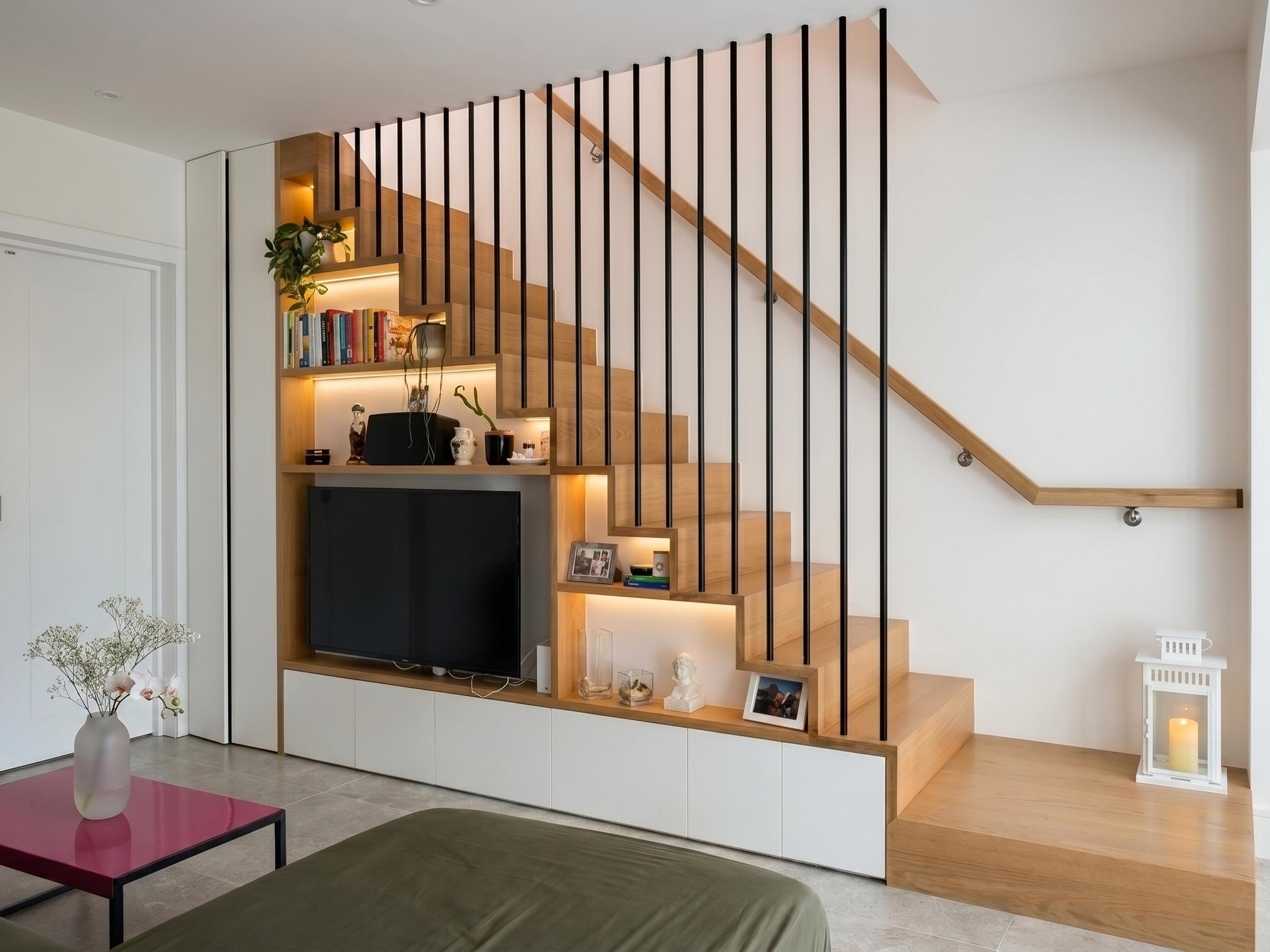 Bespoke oak staircase with black vertical balustrade and integrated joinery storage wall featuring TV, shelving and recessed LED lighting, Islington London
