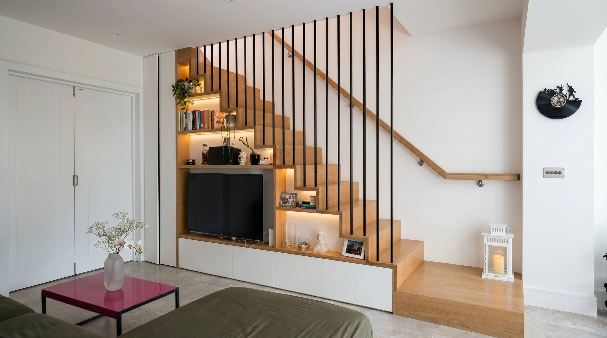 Bespoke oak staircase with black vertical balustrade and integrated joinery storage wall featuring TV, shelving and recessed LED lighting, Islington London