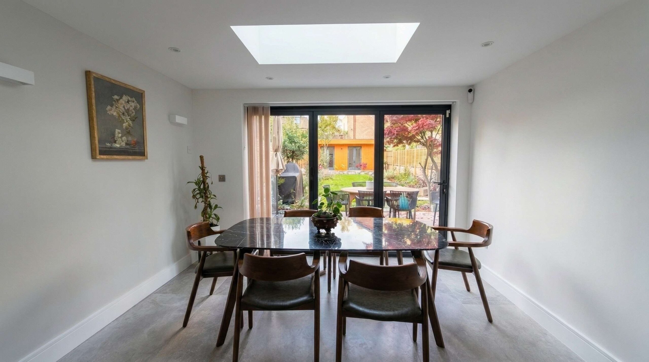 Dining room extension with flush skylight, walnut mid-century chairs around a black marble table and bifold doors framing the garden, Islington London