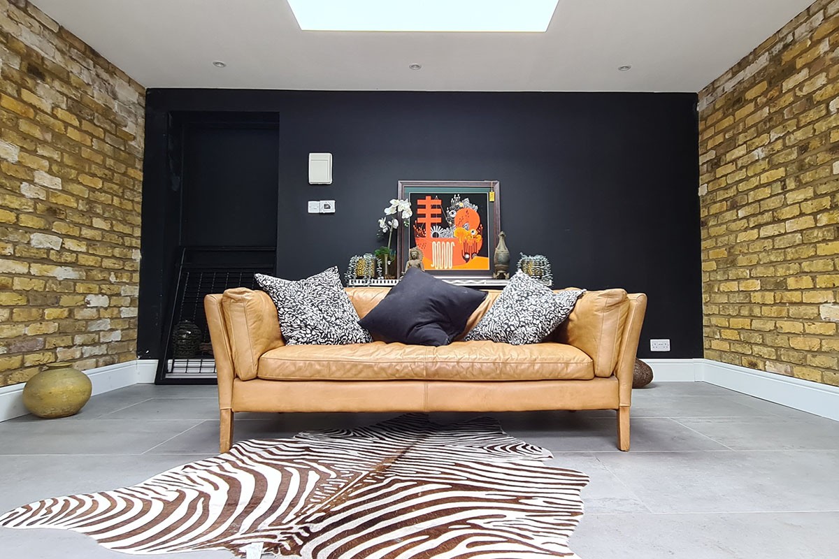 Garden room interior with tan leather sofa, exposed London stock brick wall and bifold doors framing the landscaped garden, London