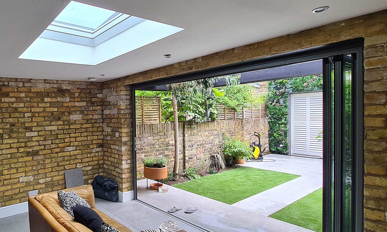 Garden room lounge interior with black feature wall, tan leather sofa, exposed London stock brick side walls and skylight overhead, London