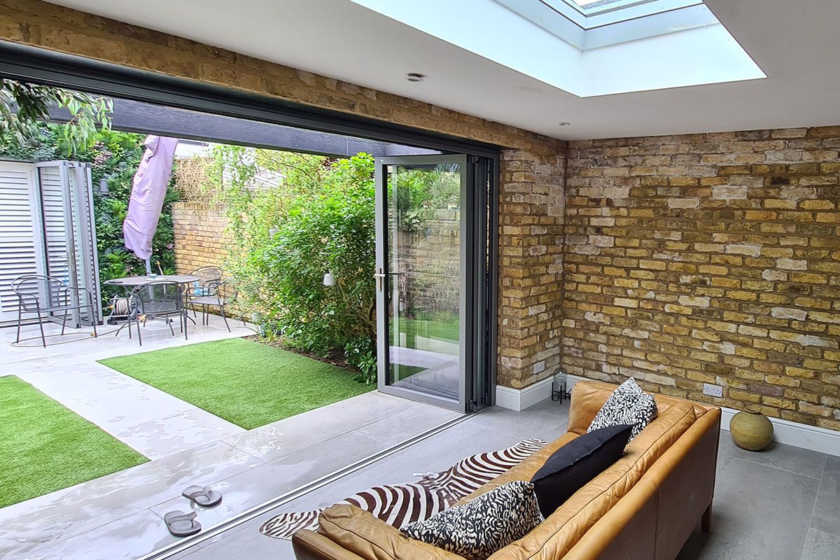 Garden room interior view with flush skylight, exposed London stock brick walls and sliding door opening onto the rear garden with timber slatted screen, London