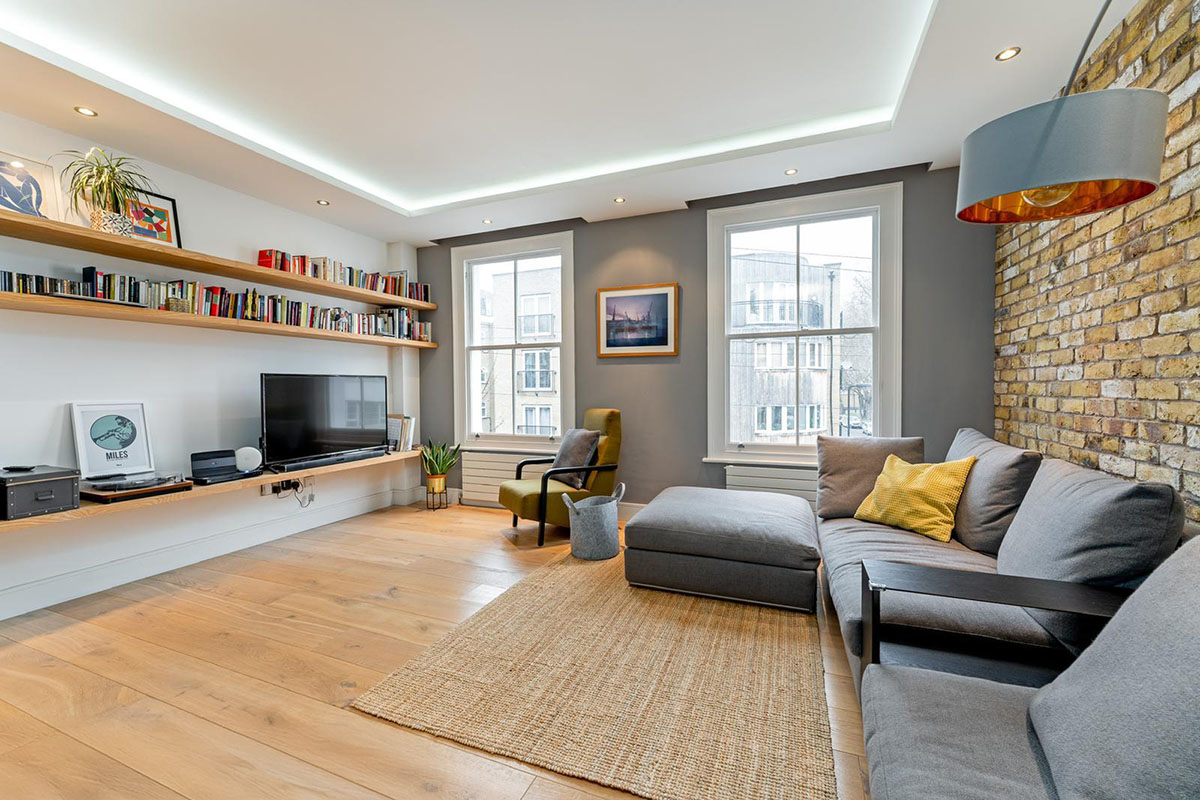 Living room renovation with exposed London stock brick wall, bespoke oak shelving and recessed cove lighting, Hackney London
