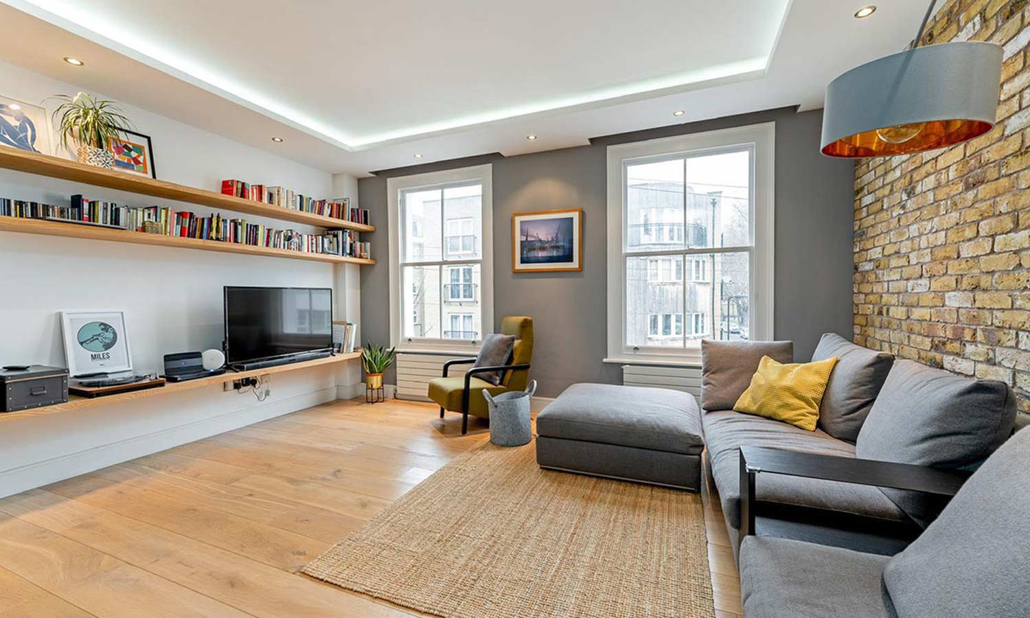 Living room renovation with exposed London stock brick wall, bespoke oak shelving and recessed cove lighting, Hackney London