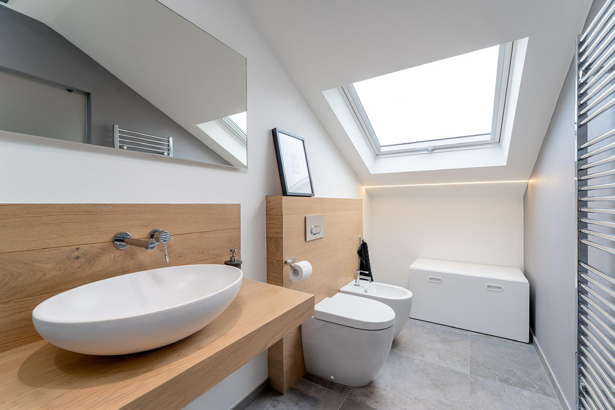 Loft bathroom with Velux skylight, oval countertop basin and oak wall cladding under sloped ceiling, Hackney London