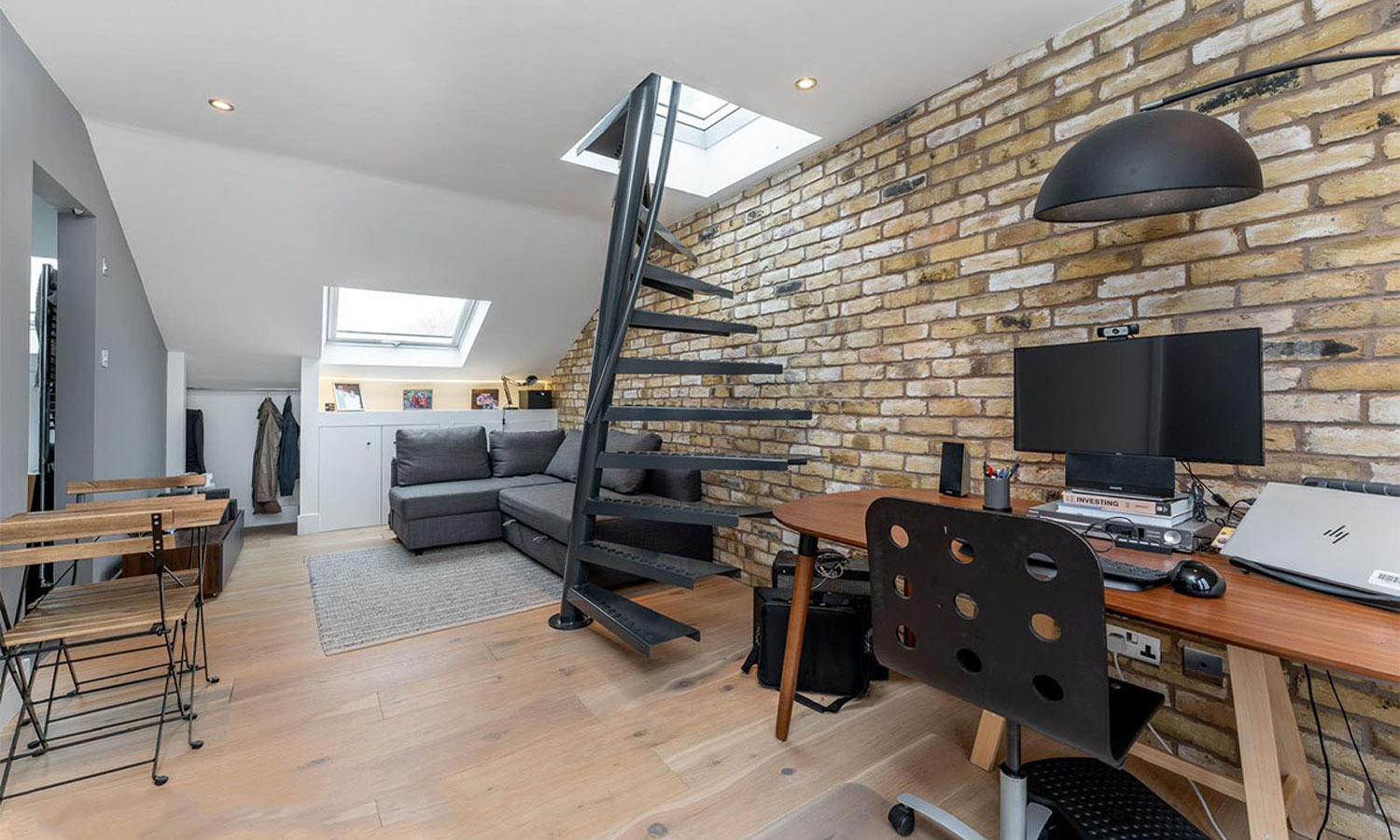 Loft conversion with black spiral staircase, exposed London stock brick wall and skylights, Hackney London