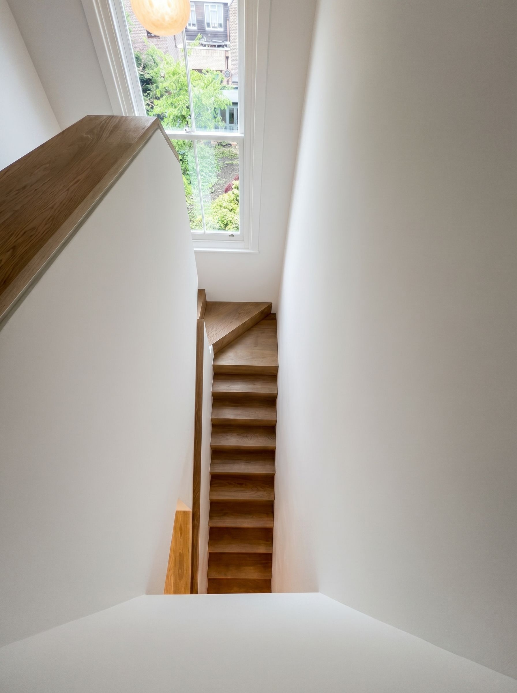 Looking down a bespoke oak loft staircase next to a restored sash window with view over Islington back gardens, London