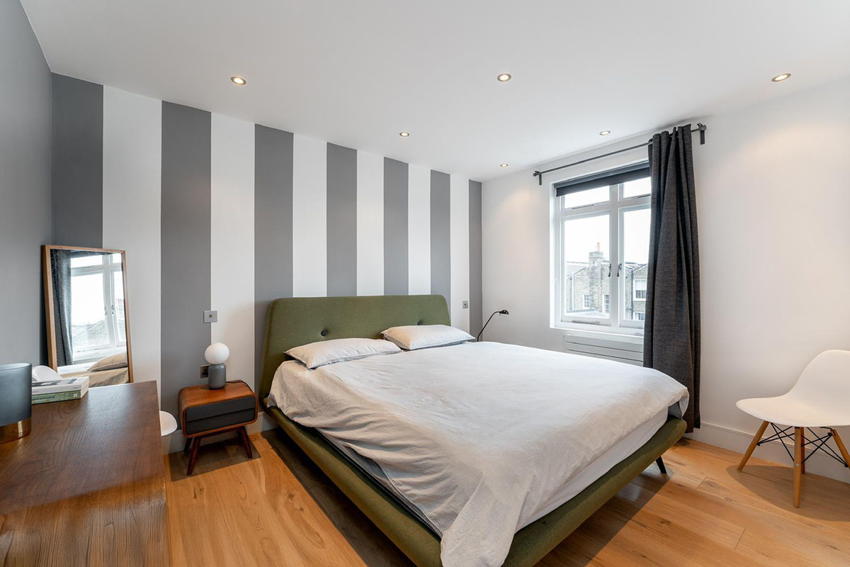 Master bedroom with striped feature wall, green upholstered bed and walnut bedside table in a Hackney home renovation, London