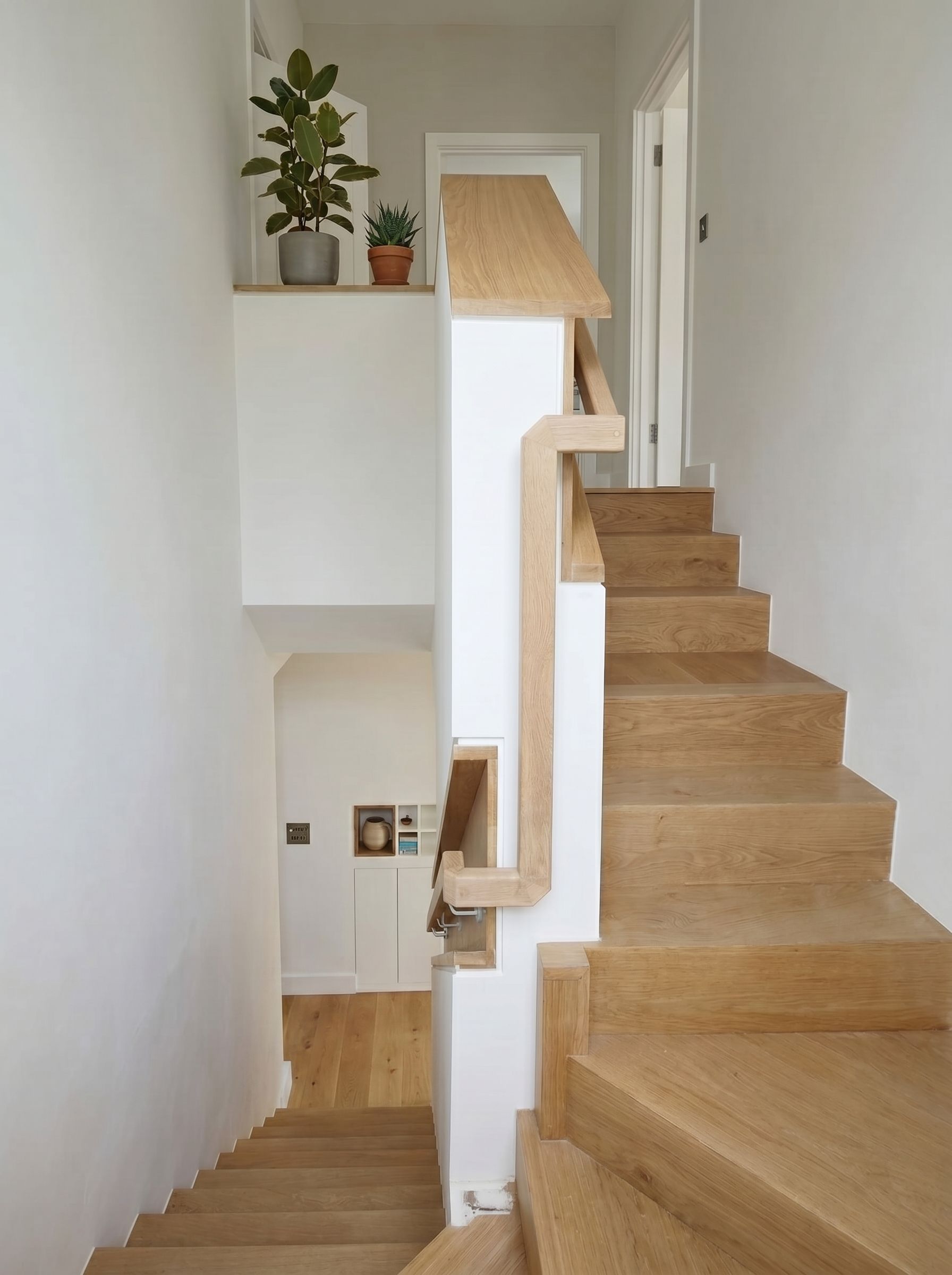 Half-landing view of a bespoke oak staircase with solid timber handrail across multiple floors of a renovated period home, Islington London