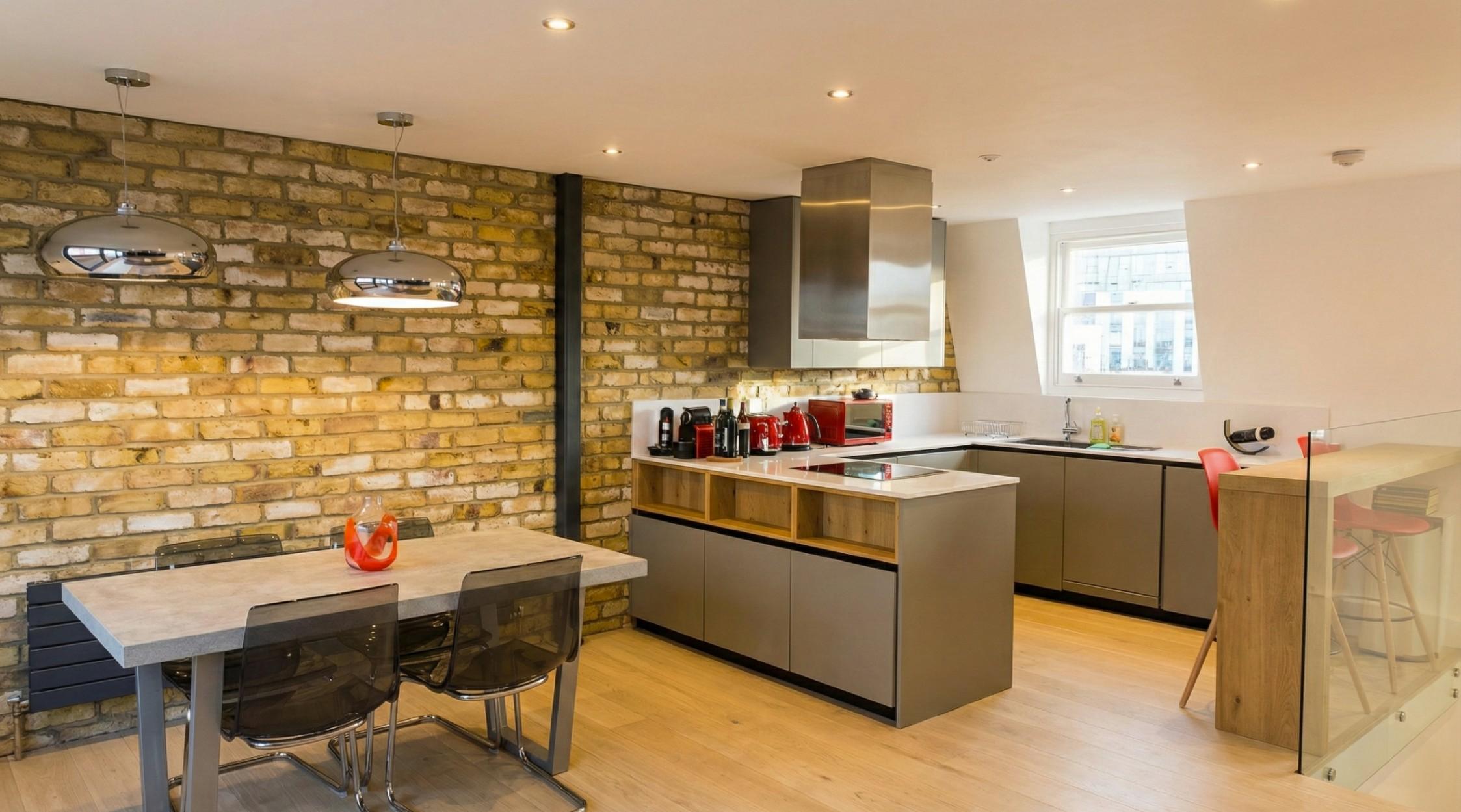 Open-plan kitchen and dining area with exposed London stock brick wall, grey matt cabinetry and stainless steel extractor hood, Fulham London