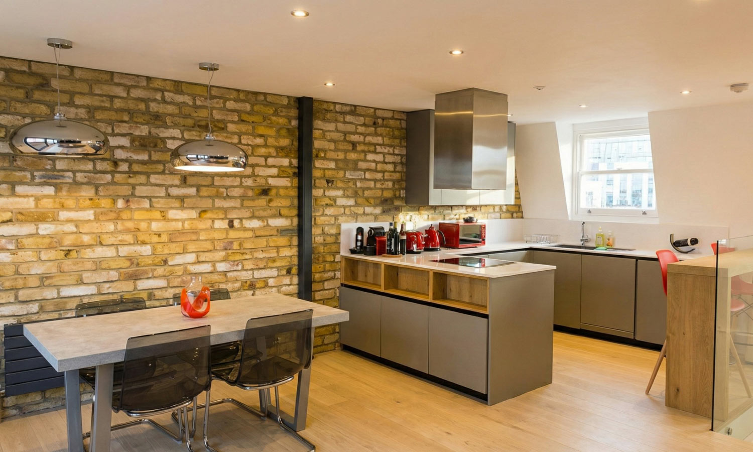 Open-plan kitchen and dining area with exposed London stock brick wall, grey matt cabinetry and stainless steel extractor hood, Fulham London