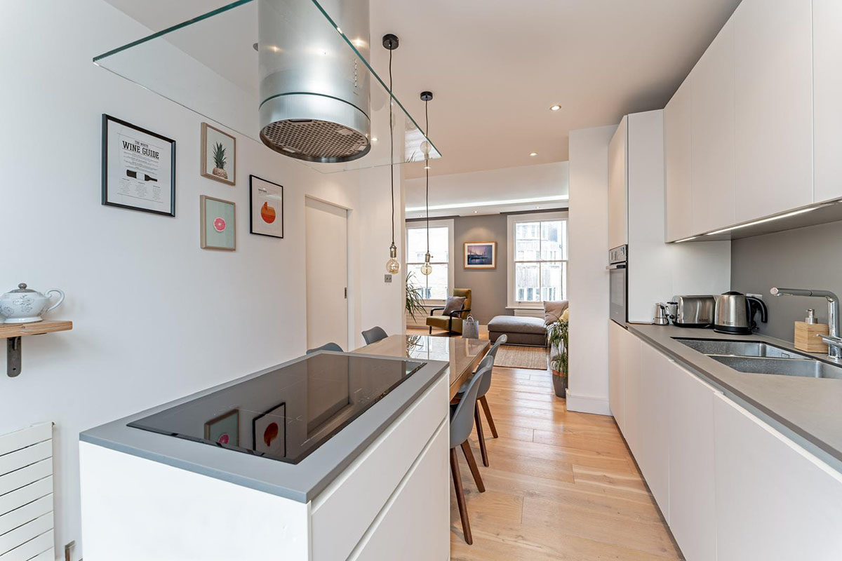 Open-plan white galley kitchen with glass extractor hood and induction hob in a Hackney apartment renovation, London