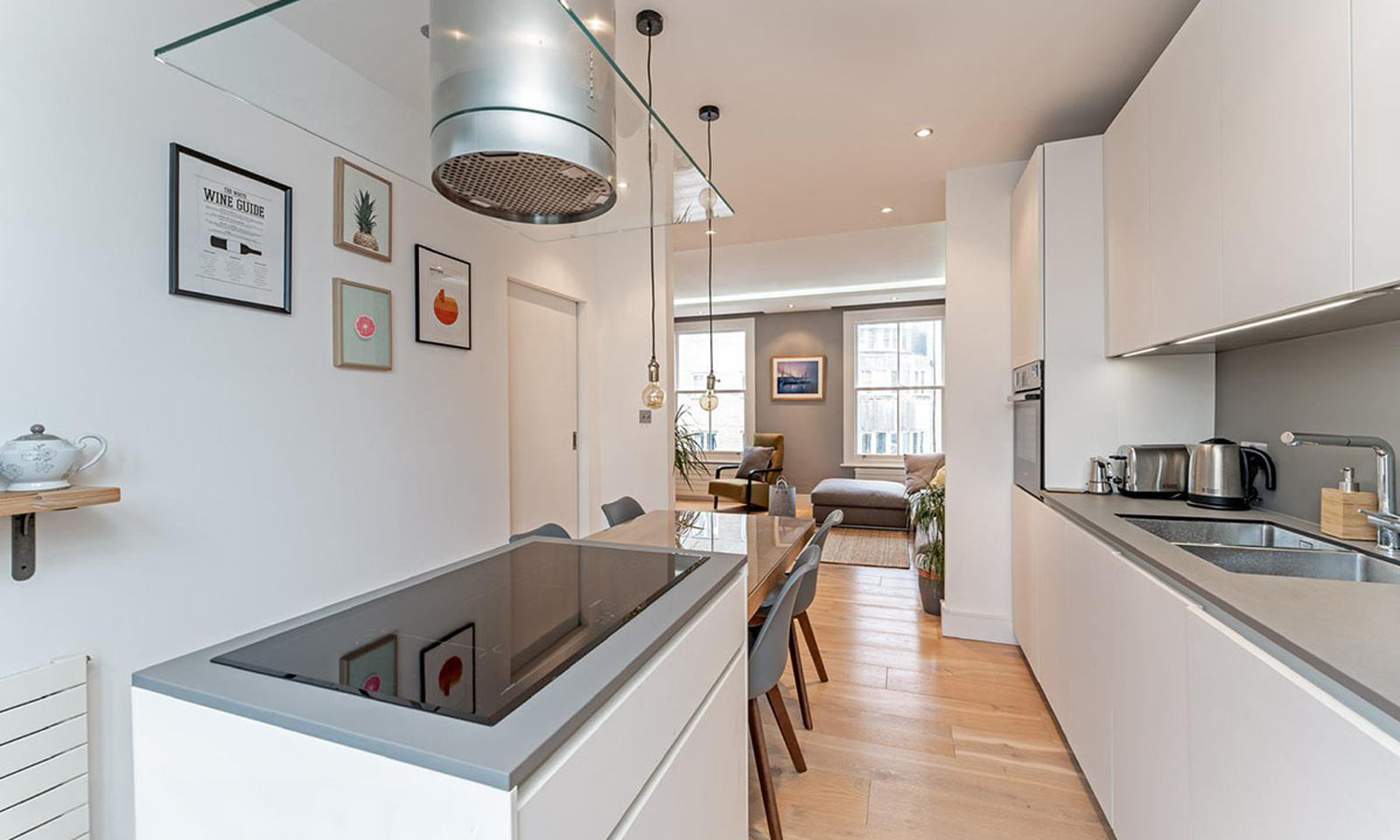Open-plan white galley kitchen with glass extractor hood and induction hob in a Hackney apartment renovation, London