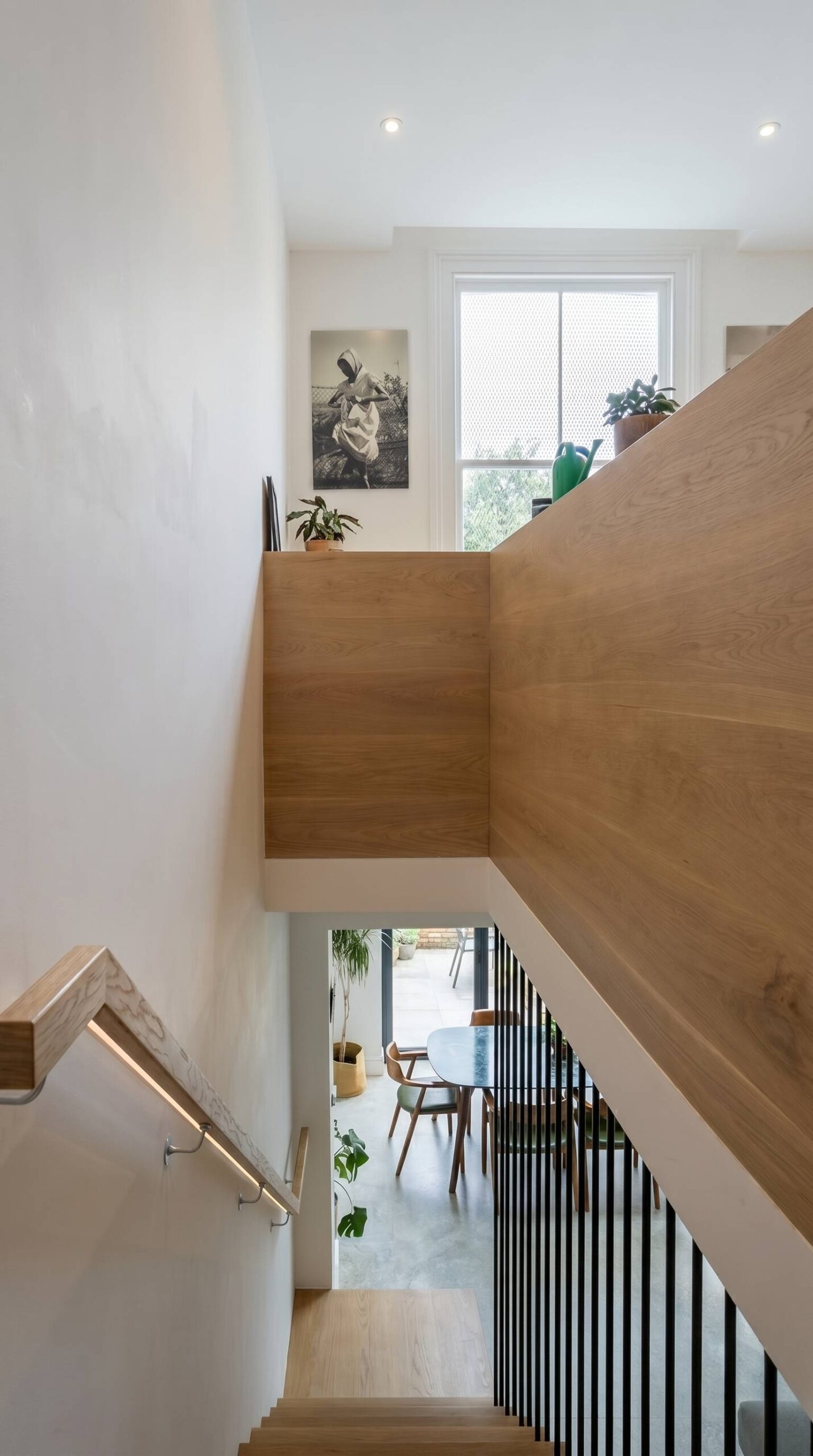 Open bespoke staircase with slim black vertical balustrade and oak panelling, framing a view down to the dining room and garden beyond, Islington London