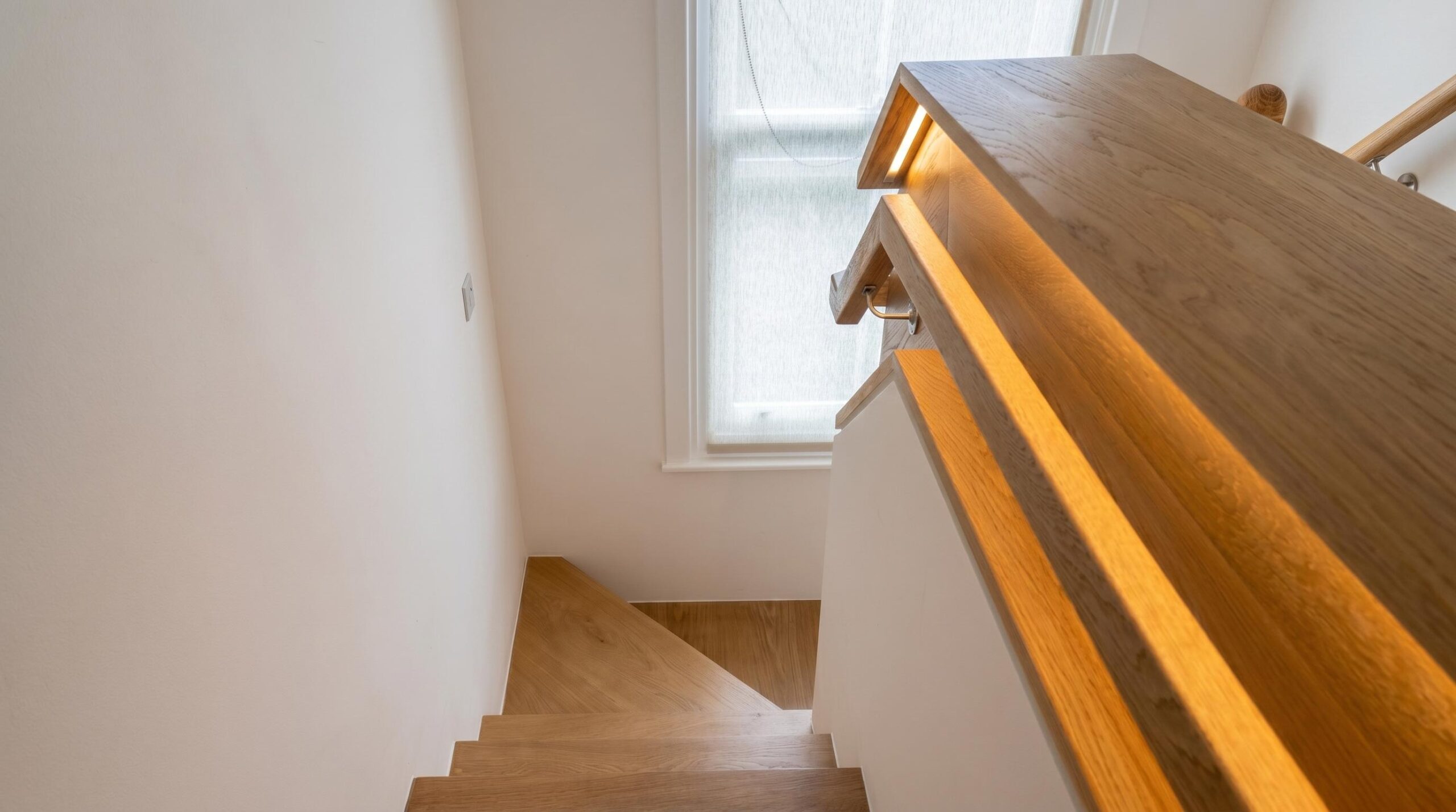 Bespoke secondary oak staircase with LED-lit solid timber handrail and original sash window in a Victorian house renovation, Islington London