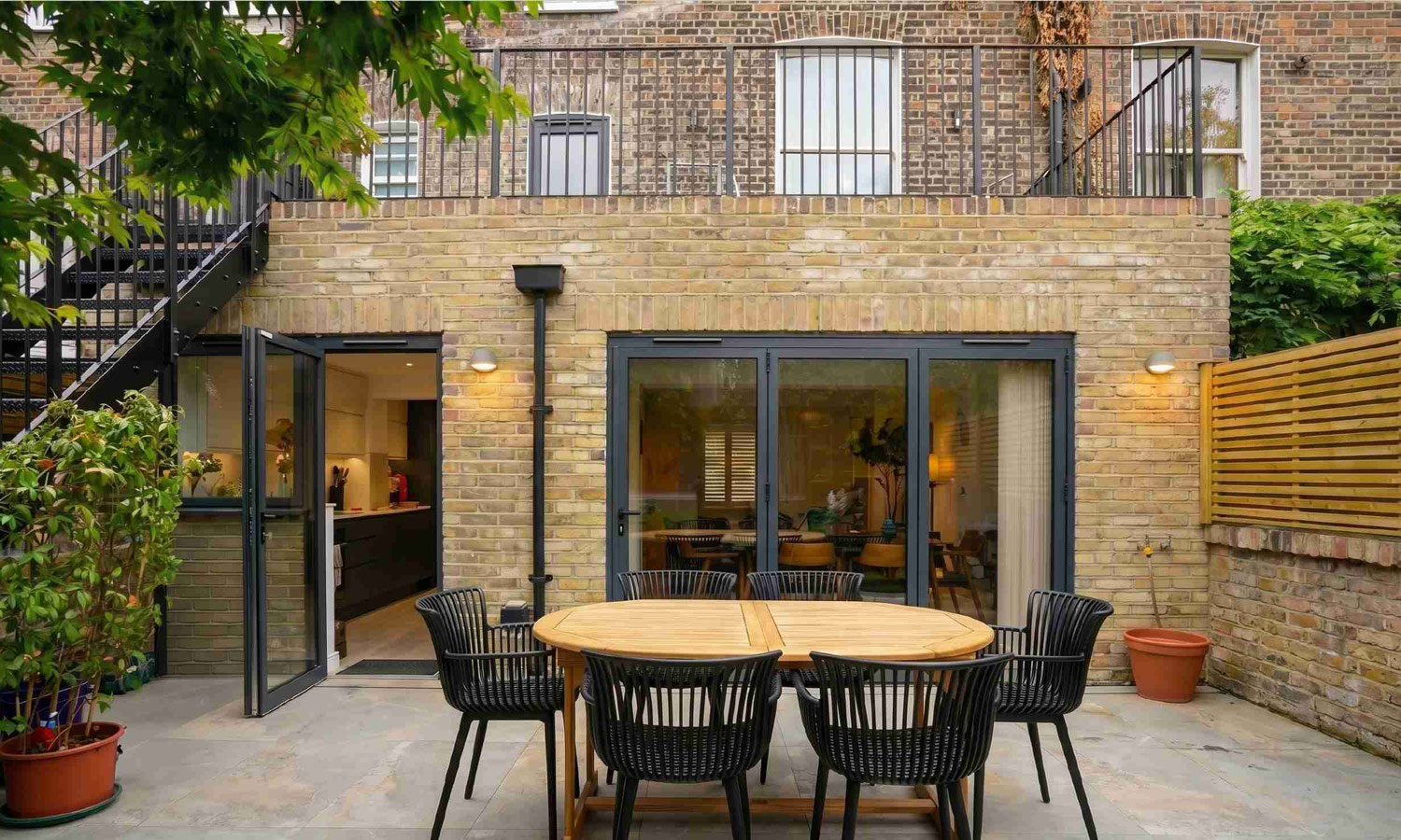 Rear view of a renovated Victorian house with lower ground floor extension, London stock brick, dark aluminium bifold doors and external metal staircase, Islington London